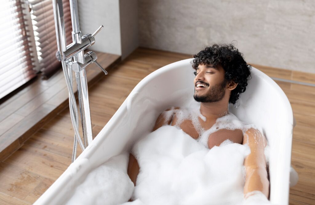 indian man laying in a bubble bath enjoying himself with his eyes closed.