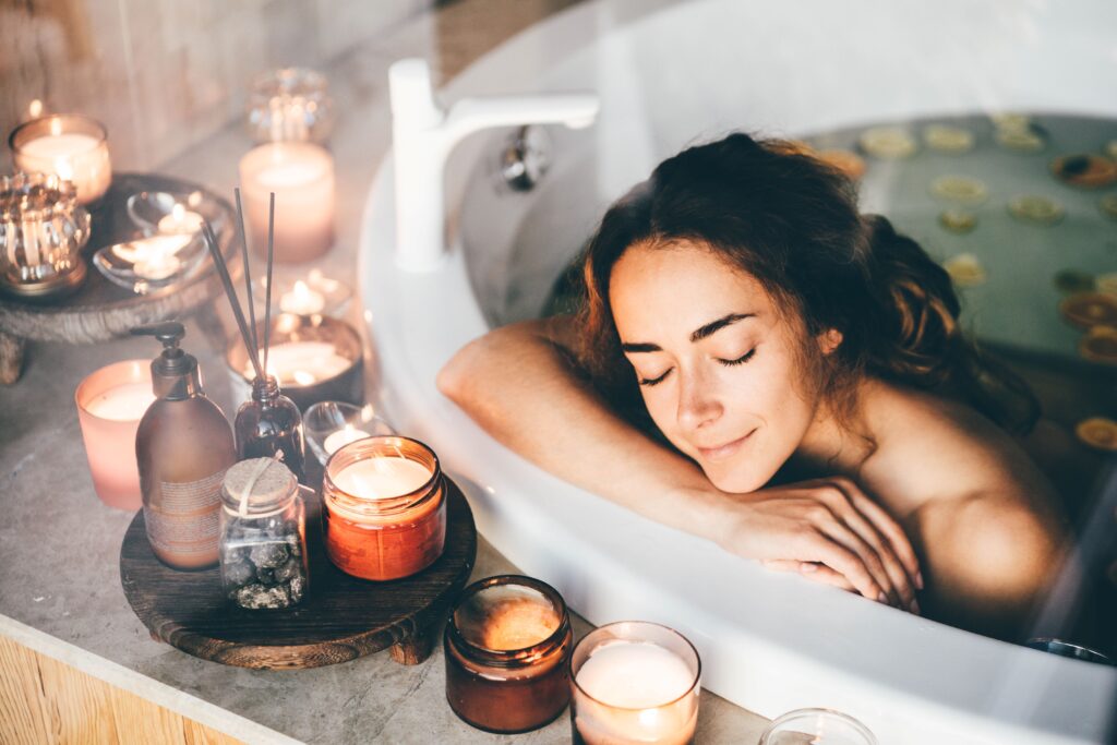 young brunette woman laying in bathtub with her head resting on the edge, enjoying candles