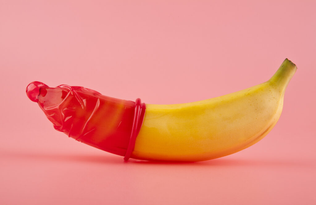 yellow-banana-with-a-red-condom-on-the-tip-against-a-pink-background