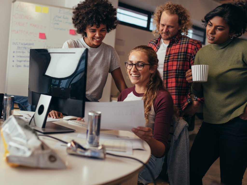 A group of young adults working at a fem-tech startup, sitting around a computer looking at paperwork. 