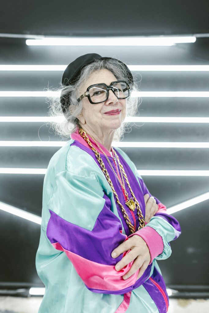 A fashion forward menopausal woman stands in a multicolored jacket, smiling at the camera.