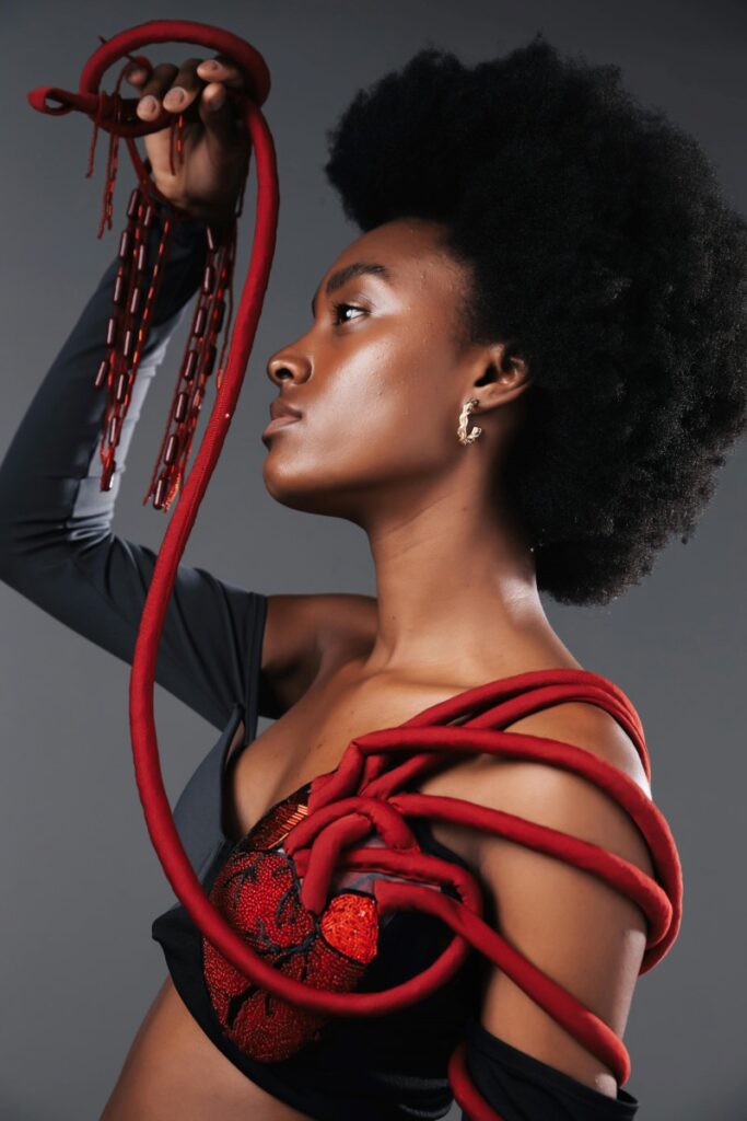 Black woman holding red rope attached to arm and top she is wearing