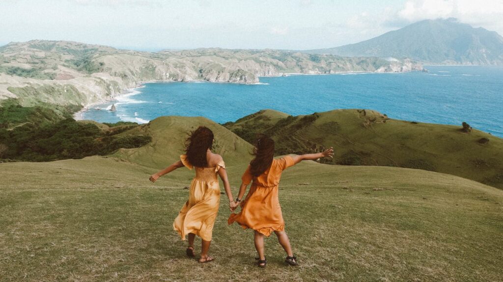 Two young women holding hands on a cliff overlooking the ocean