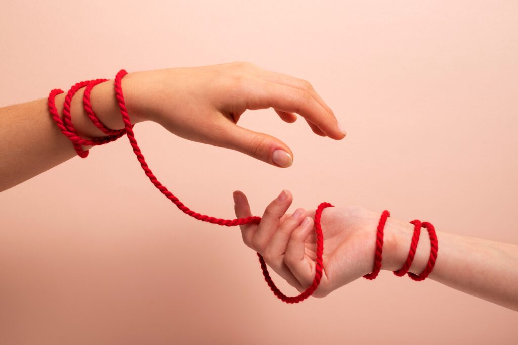 Two hands intertwined with red shibari rope. 