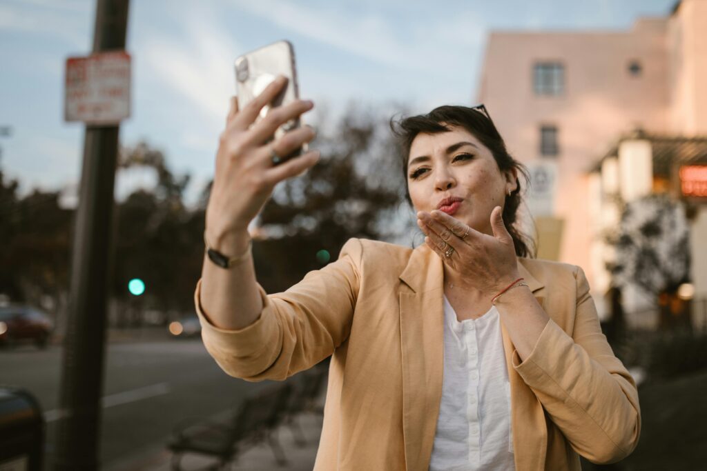 A webcam model is kissing goodbye to a client on her cellphone. She is on the street. 