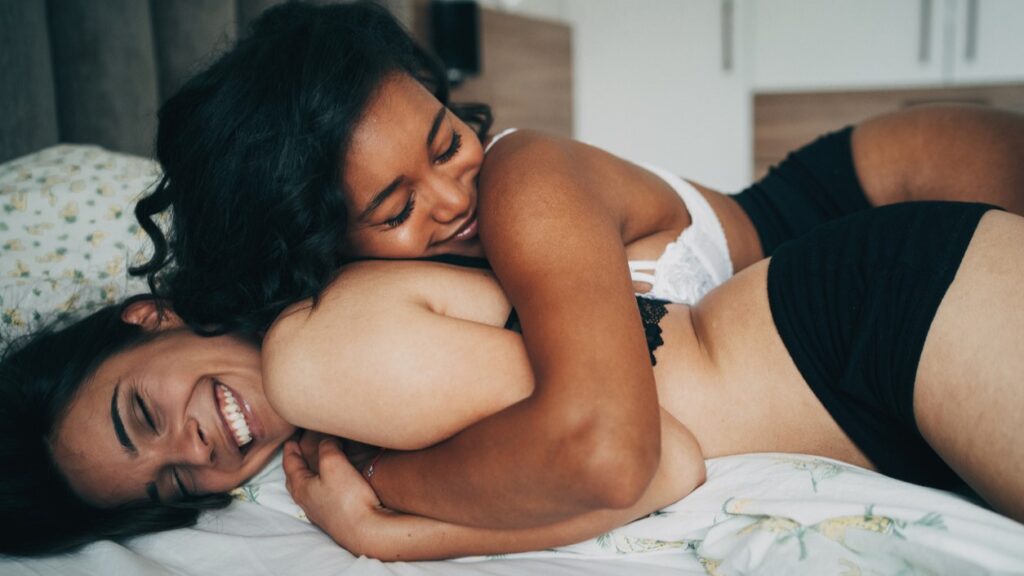 lesbian mixed race couple in bed smiling and hugging with their eyes closed