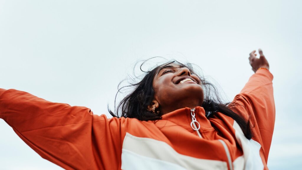 A young Indian woman representing singlehood holds her arms up to the sky with her eyes closed