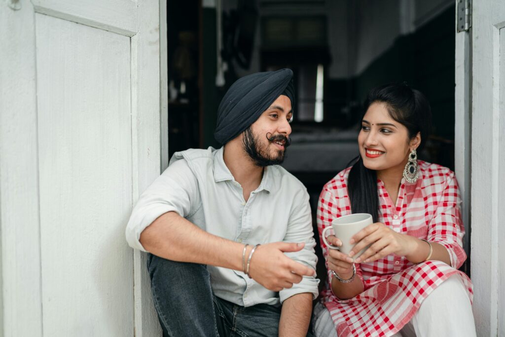 A middle-eastern couple sitting in their doorway. They look happy and engaged. She is holding a coffee mug. 