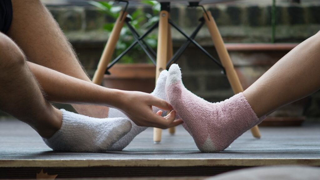 White male appears to tickle a foot wearing cozy pink socks.