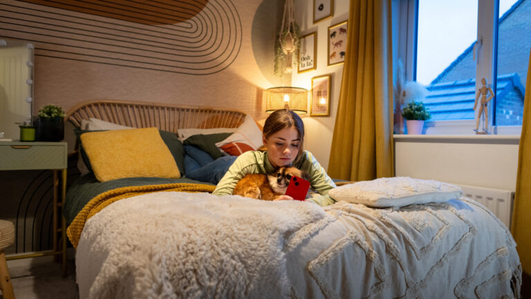 Full shot of a young girl lying on her bed with her mobile phone, she is embracing the dog in between her arms. The location is their home located in North East of England in Newcastle Upon Tyne.