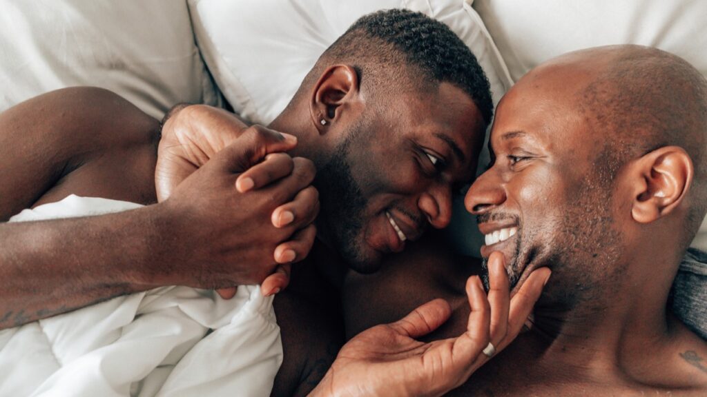 Black gay couple in bed smiling and looking into each others eyes