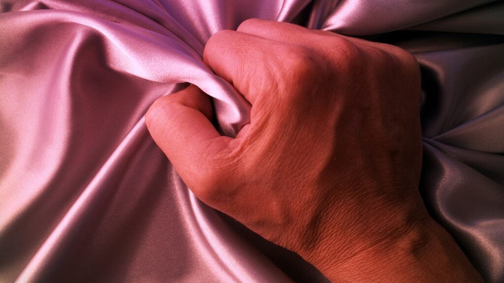 Man's hand grabs pink satin sheet