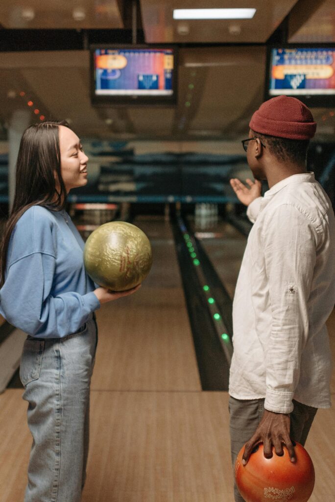 Two friends bowling together. The female is smiling while it appears the male is motioning at the lanes. 