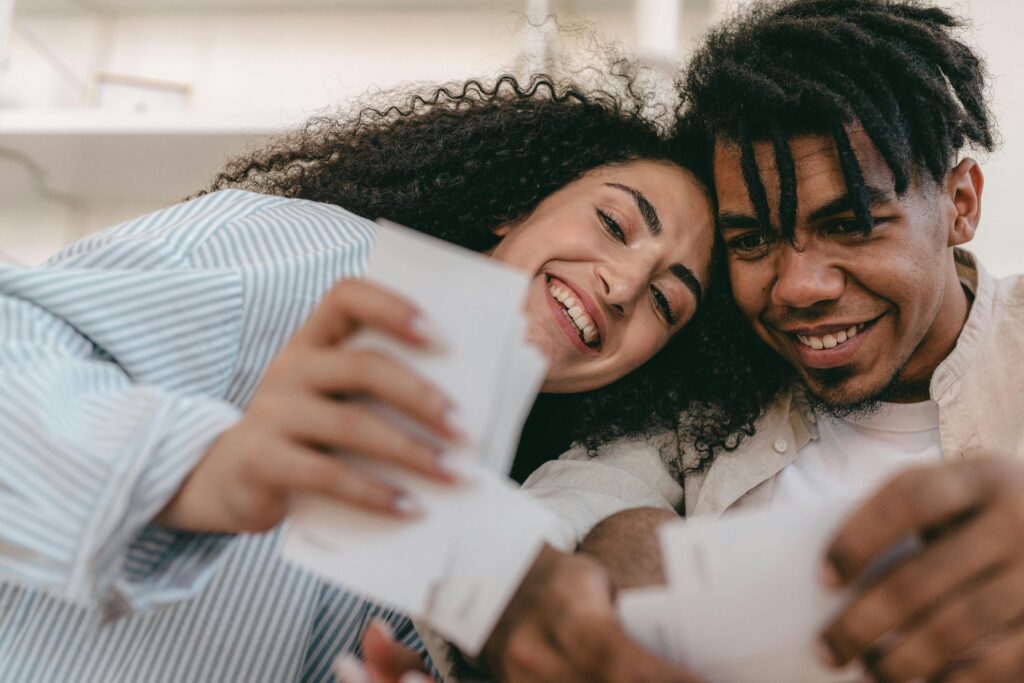 A diverse couple are smiling and looking back at pictures of themselves. They are reflecting on the good memories. 