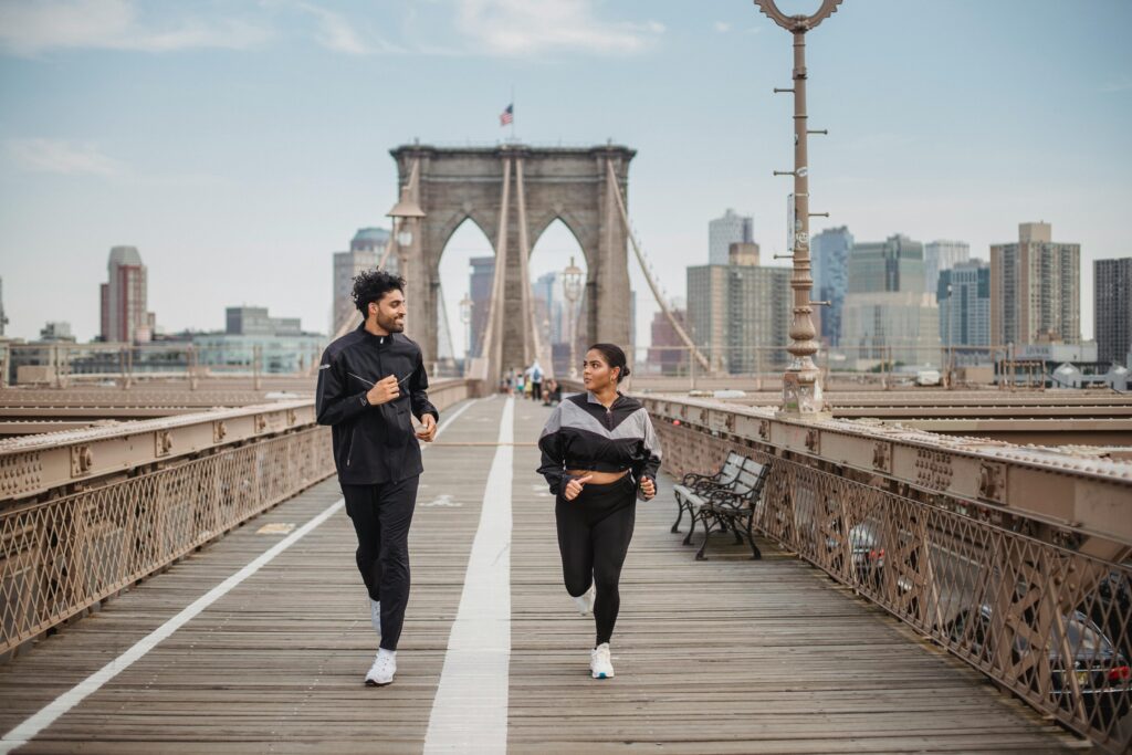 A couple jogging together across a bridge. They are looking at each other, smiling. 