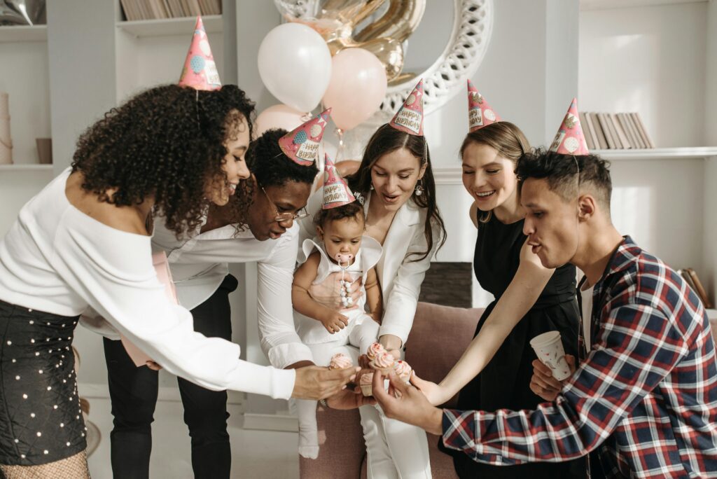 A group of young adults all holding birthday cupcakes in front of a baby representing a polyamorous family dynamic