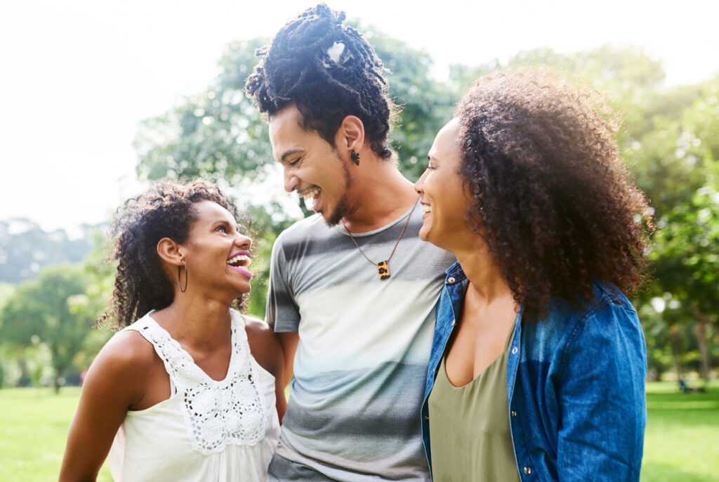 A diverse man with two diverse women, all smiling at each other and embracing one another. 