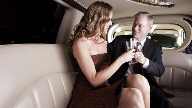 A young woman in a small dress sits next to an older man holding drinks in a limo