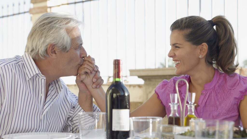 Older man holds and kisses the hand of a young woman at a restaurant table