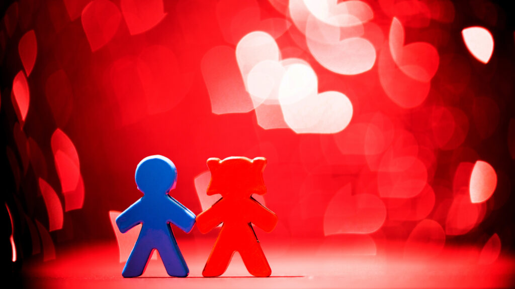 A red and blue couple figurines on a shiny background. They appear to be "holding hands". 