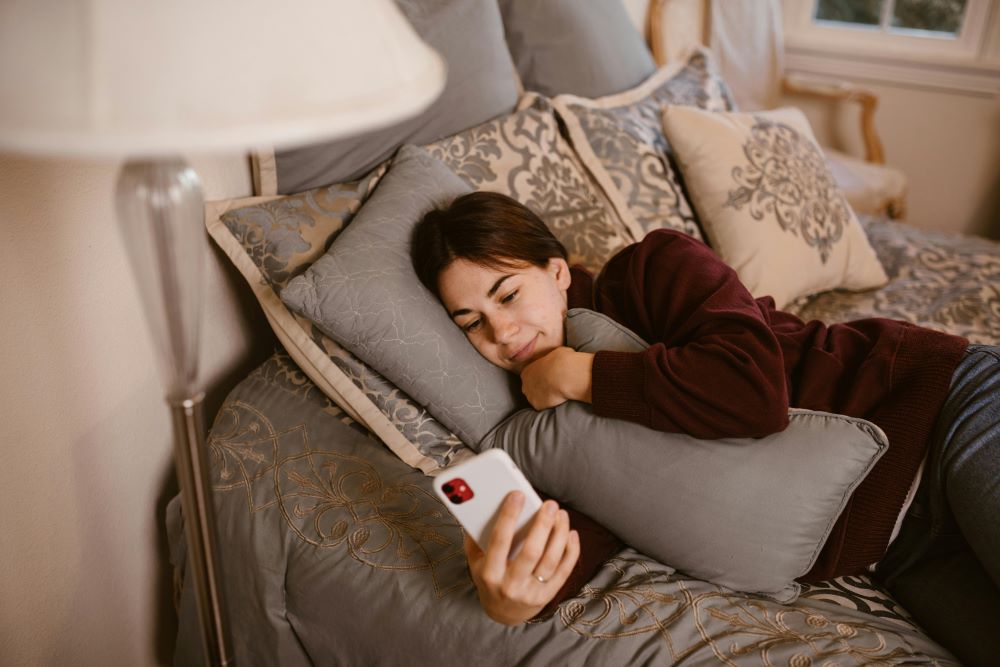 female snuggled on bed with pillow looking lovingly at her phone.