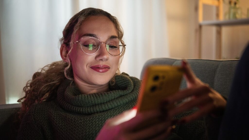 Young woman lying on couch appears happy while texting