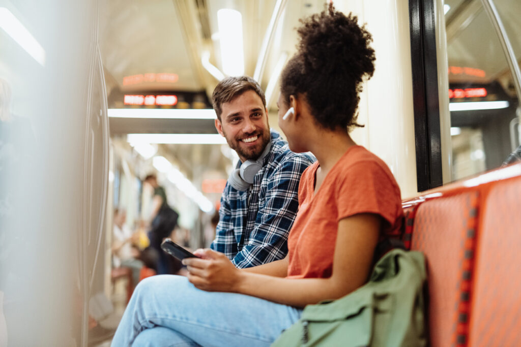 A young man flirts with a young woman on a public transportation bus or train. 