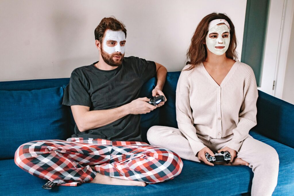 A young couple, both wearing face masks, playing video games together.