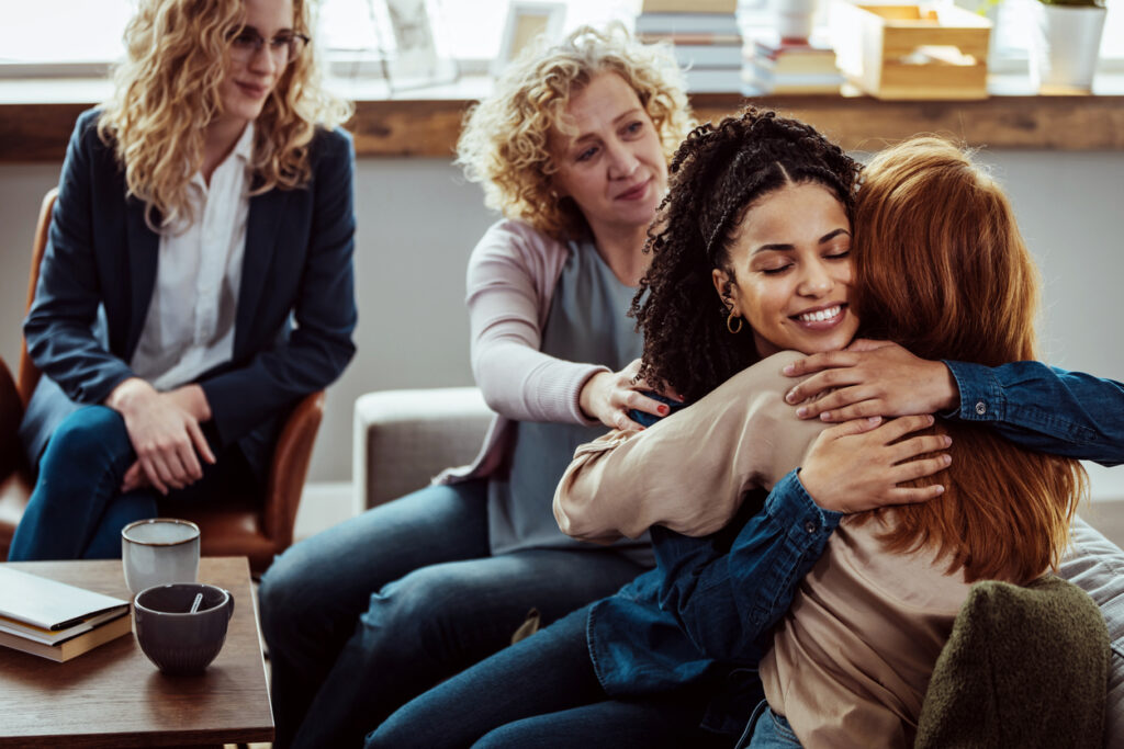 A group of therapists support each other, with one giving another a hug.