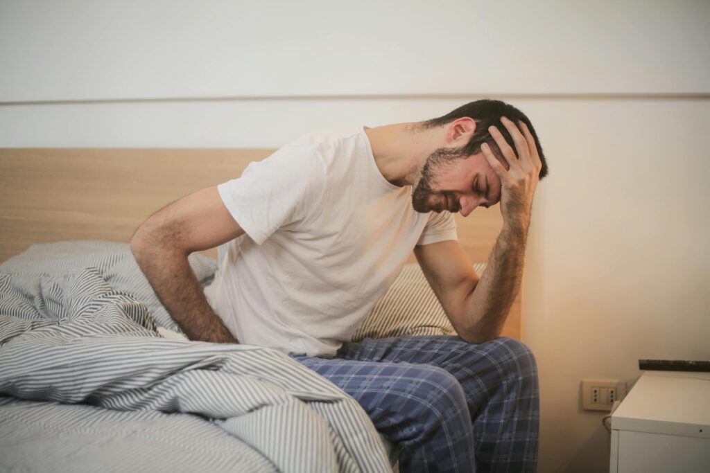 Young man in sleepwear who looks likes he's suffering, sitting on the edge of the bed.