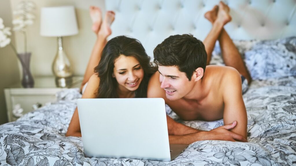 Couple in bed watching their laptop and smiling