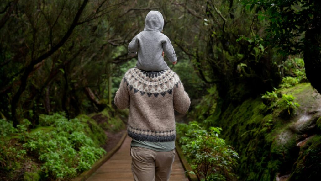 man with baby on shoulders walking down a forest path