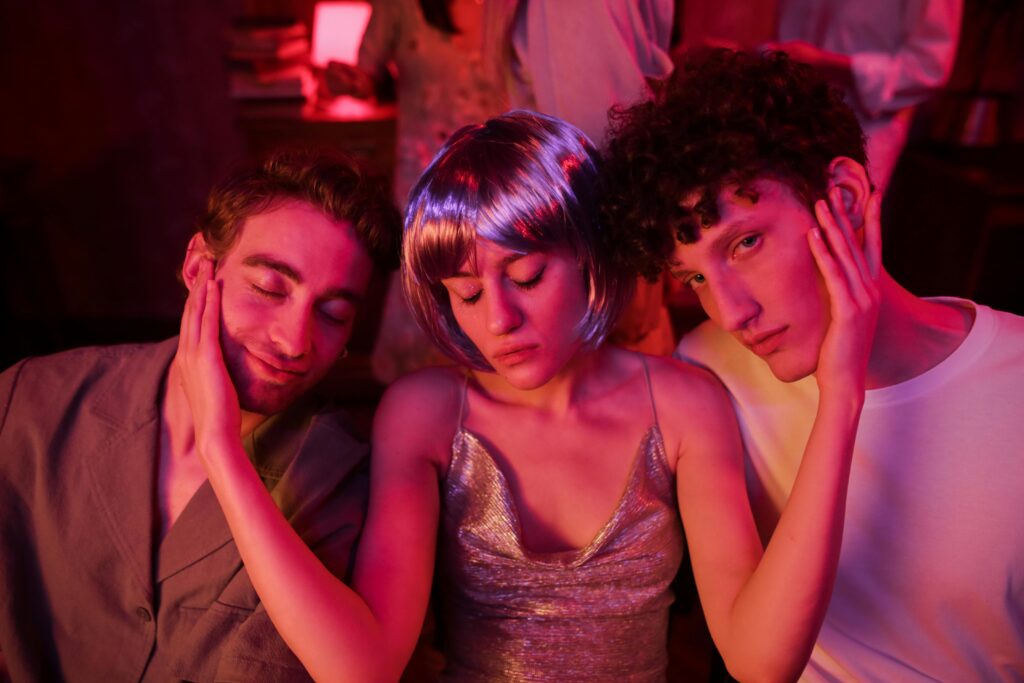 a woman in a purple glittery tank and purple wig sitting between two men at a night club